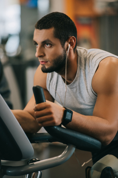 handsome young man working out on stationary bicycle at gym - 写真・画像