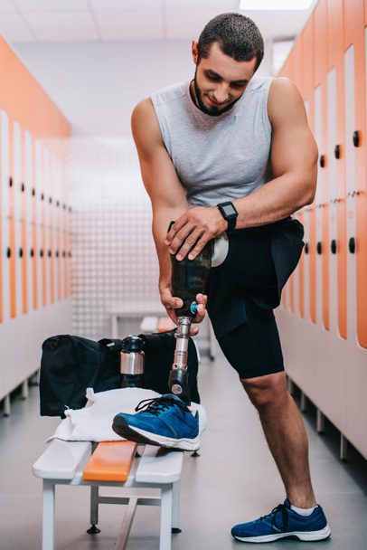 athletic young sportsman putting on artificial leg at gym changing room - Fotó, kép