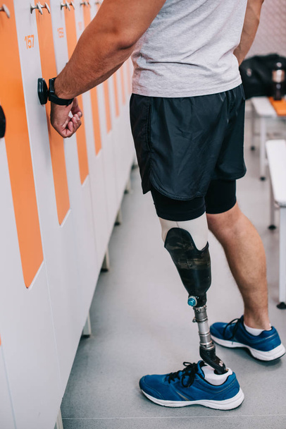 Oříznout záběr sportovce s umělou nohou otevření skříňky s elektrický klíč na zápěstí v šatně tělocvičny - Fotografie, Obrázek