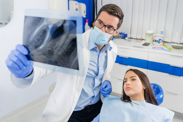 Mulher jovem paciente olhando sua imagem de raio-x no dentista
. - Foto, Imagem