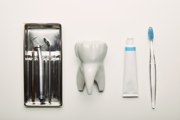vlakke leggen met RVS tandheelkundige instrumenten in container, tand model, tandenborstel en pasta gerangschikt op wit tafelblad - Foto, afbeelding