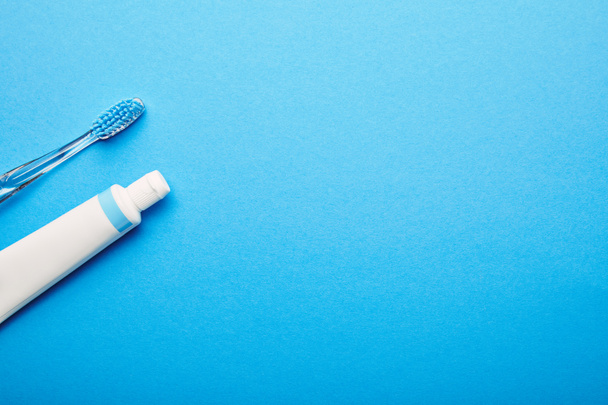 top view of toothbrush and toothpaste arranged on blue backdrop, dentistry concept - Foto, Bild