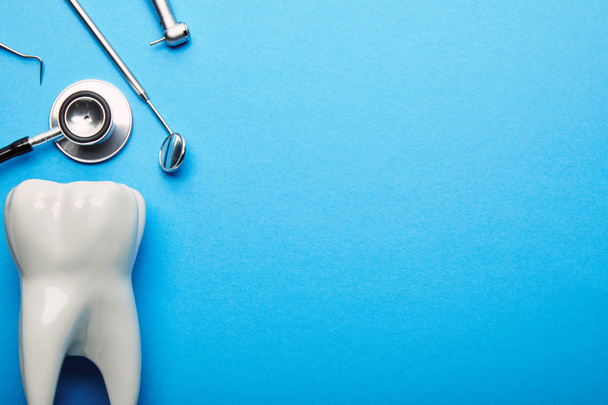 vlakke leggen met tand model, stethoscoop en steriele tandheelkundige instrumenten gerangschikt op blauwe achtergrond - Foto, afbeelding