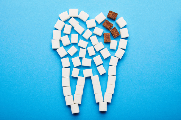 vista superior de cubos de açúcar branco e marrom dispostos em sinal de dente no fundo azul, conceito de cárie dentária
 - Foto, Imagem