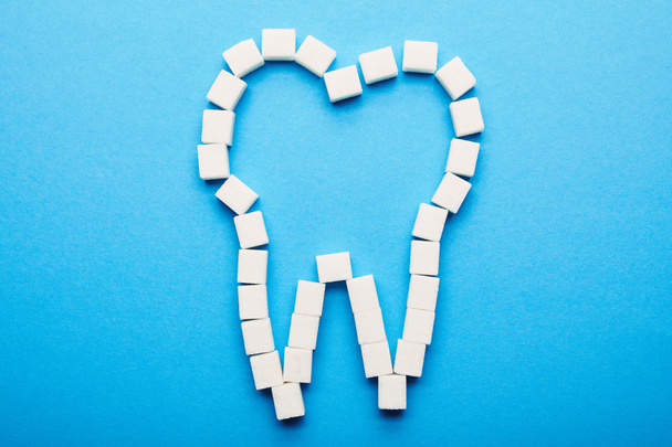 κάτοψη του λευκή ζάχαρη σε κύβους διατεταγμένα σε σημάδι των δοντιών σε μπλε φόντο, οδοντιατρική φροντίδα έννοια - Φωτογραφία, εικόνα
