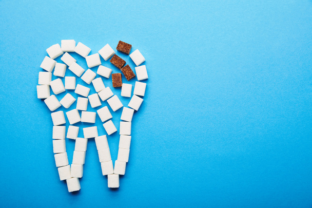 vista dall'alto di cubetti di zucchero bianco e marrone disposti in segno di denti su sfondo blu, concetto di carie dentale
 - Foto, immagini