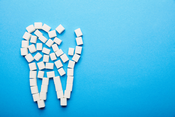 vista superior de los cubos de azúcar blanco dispuestos en el signo dental sobre fondo azul, concepto de cuidado dental
 - Foto, Imagen
