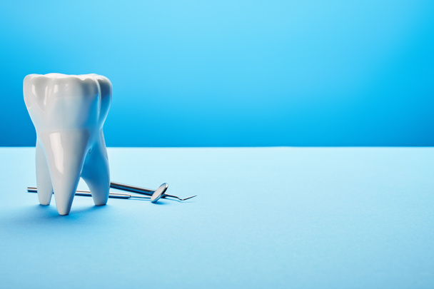 Vista de cerca del espejo dental estéril, la sonda y el modelo de dientes dispuestos en el fondo azul
 - Foto, Imagen