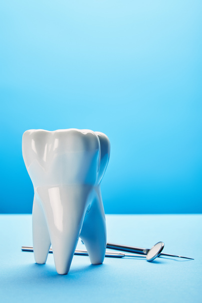 close up view of sterile dental mirror, probe and tooth model arranged on blue backdrop - Zdjęcie, obraz