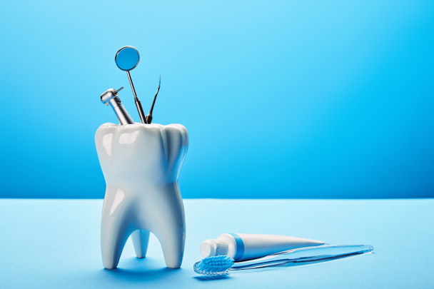 vista ravvicinata di modello di dente bianco, spazzolino da denti, dentifricio e strumenti dentali in acciaio inox su sfondo blu
 - Foto, immagini