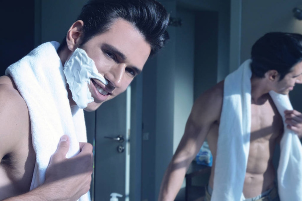 A handsome man lacks his beard to have smooth and hairless skin. Half face has put shaving foam to shave better and half has shaved his face. Concept of: cleaning, beard, beauty. - Foto, imagen