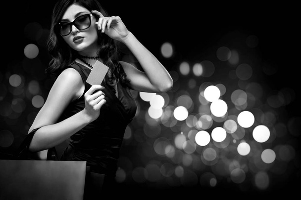 Christmas or Black friday sale concept. Shopping woman holding bag on dark background with bokeh in holiday. BW photo. - Zdjęcie, obraz