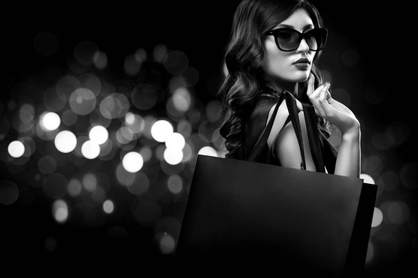 Christmas or Black friday sale concept. Shopping woman holding bag on dark background with bokeh in holiday. BW photo. - Foto, immagini