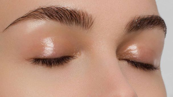 Macro shot of beautiful eyes of the girl with beautiful eyebrows and long eyelashes. One eyebrow is raised. Brown shades in a make-up. Cosmetology, Spa, correction, injections - 写真・画像