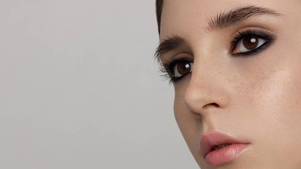 Closeup of beauty woman with clean shiny skin and dark smoky shadows on brown eyes. Extremely long eyelashes and tender lips, freckles. Fashion, spa, cosmetology, cosmetics, makeup - Φωτογραφία, εικόνα