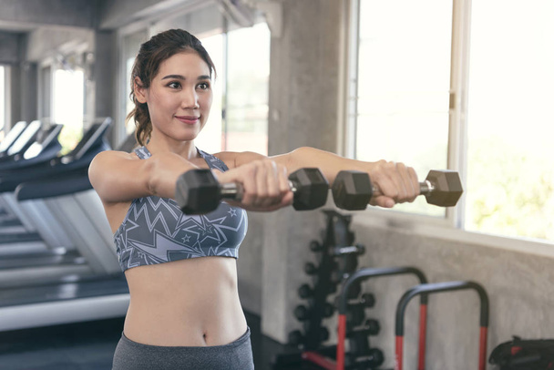 Genç Asyalı kadın spor salonunda dambılları kaldırıyor. sağlıklı yaşam tarzı ve çalışma motivasyonu kavramı. - Fotoğraf, Görsel