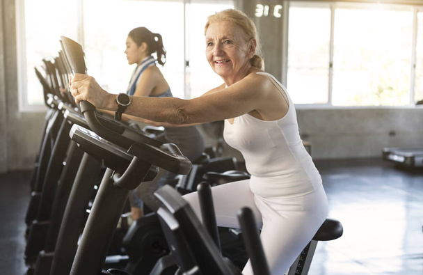 Senior žena cvičení spinning kolo ve fitness tělocvičně. starší zdravý životní styl koncept.  - Fotografie, Obrázek