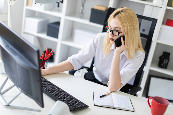 Uma jovem trabalhando em um computador no escritório e falando ao telefone
. - Foto, Imagem