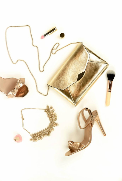 Flat lay, top view female high heels shoes sandals golden color, accessories clutch bag,  necklace and make up cosmetics on a white background. Glamour background.  Copy space . - Φωτογραφία, εικόνα