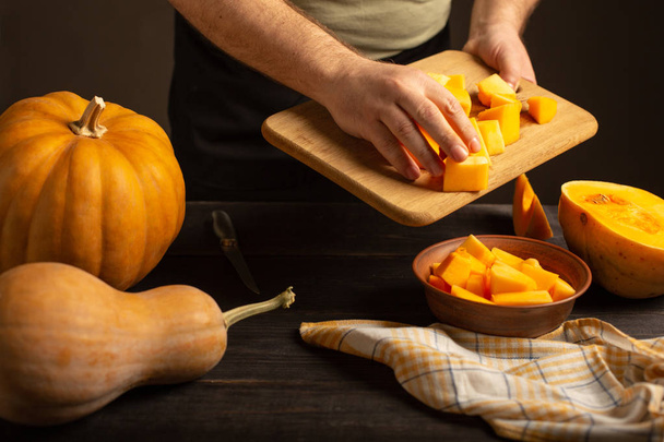 Cook throws slices of pumpkin from a cutting board into a deep bowl. - Foto, immagini