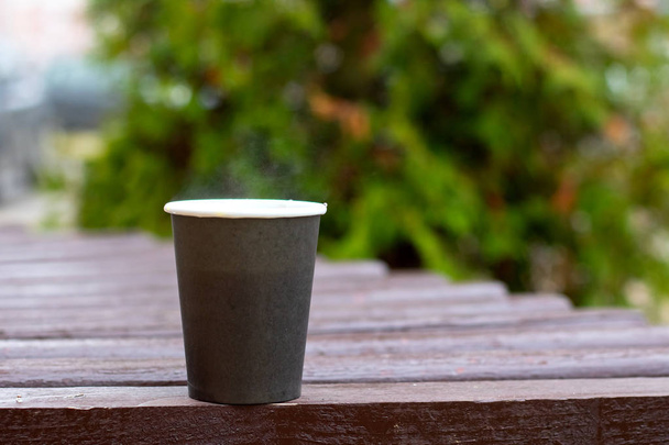 Grijs plastic beker met koffie op de achtergrond van bijkantoren in park - Foto, afbeelding
