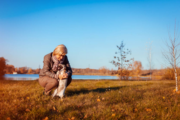 Master walking pug dog in autumn park by river. Happy woman hugging pet outdoors - Photo, image