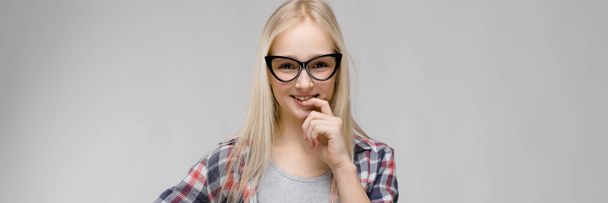 Beautiful teen girl with long hair and wearing glasses. A teenage girl in a plaid shirt and a gray T-shirt. A teenage girl leaned her finger to her lips. - 写真・画像