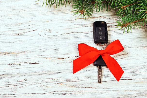 クリスマスの車のキーのためのギフト。木製の素朴なヴィンテージ背景に存在として赤い弓と車のキーのクローズ アップ ビュー. - 写真・画像