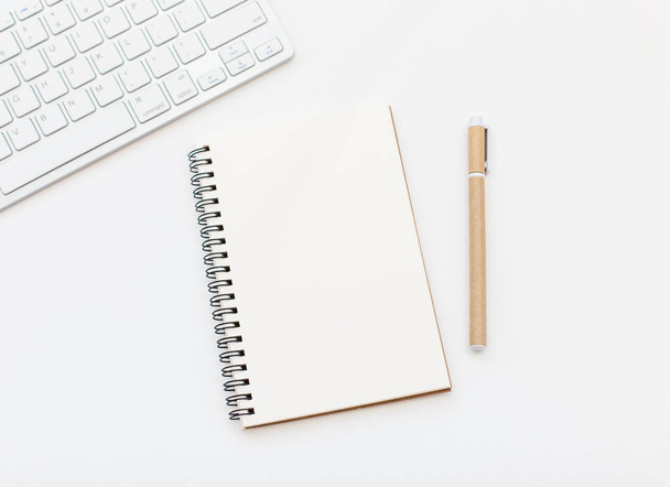 Cuaderno en blanco, pluma y teclado sobre fondo blanco. Espacio del bloc de notas para la entrada de texto
 - Foto, imagen
