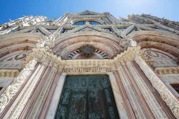 Looking up at the pink and white marble and magnificent sculptures adorning the fascia of the 13th century cathedral in Siena - Photo, Image