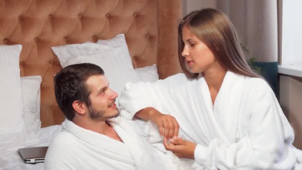 Όμορφο ζευγάρι χαλαρωτικό μαζί στο κρεβάτι, φορώντας μπουρνούζια - Πλάνα, βίντεο
