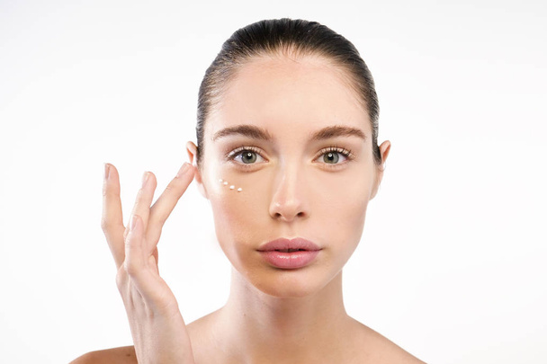 caucasian woman applying anti-aging cream on face and looking at camera - Photo, image