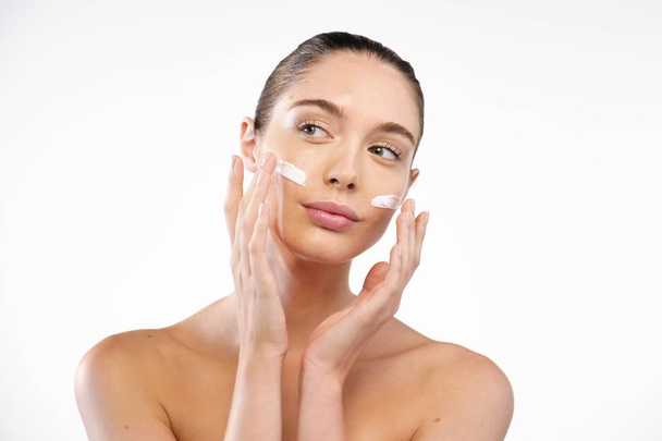 portrait of brunette woman applying moisturizing cream on face  - Φωτογραφία, εικόνα