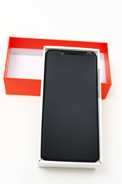 Το μαύρο smartphone είναι στο λευκό πλαίσιο. Είναι κοντά στην κορυφή πορτοκαλί. - Φωτογραφία, εικόνα