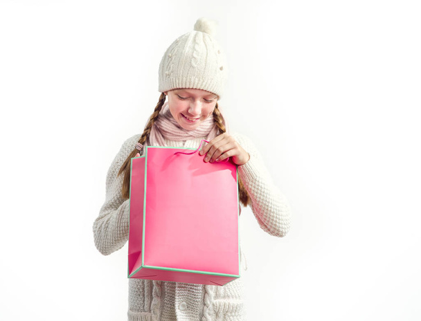 Girl in a winter hat and a warm sweater with a pink bag in her hands. Christmas gifts and purchases. - Zdjęcie, obraz