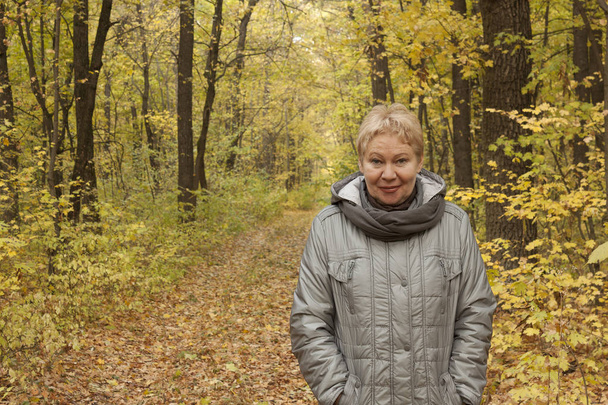 A woman of mature age in the forest with yellow leaves. Autumn, October - Photo, Image