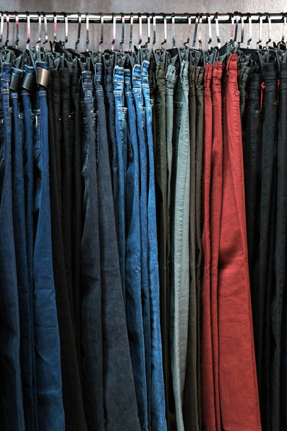 Джинсові штани різних кольорів на вішалках в магазині одягу. Тло для дизайну на тему моди або другої руки. Концепція шопінгу та продажів
. - Фото, зображення