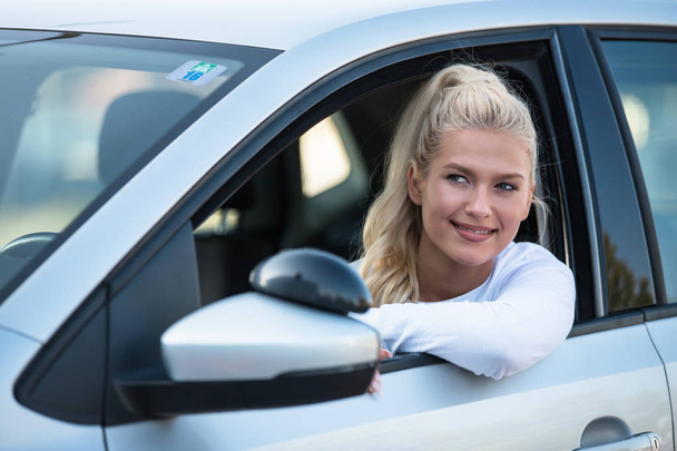 Νεαρή γυναίκα οδήγηση μαθητή που κάθεται σε ένα αυτοκίνητο. Πορτραίτο του μια όμορφη γυναίκα σε ένα αυτοκίνητο, κοιτάζοντας έξω από το παράθυρο και να χαμογελά. Σχολή οδηγών - Φωτογραφία, εικόνα