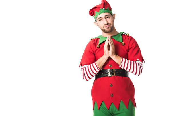 Человек в рождественском костюме эльфа держит ладони вместе, как жест пожалуйста и с обнадеживающим выражением изолированы на белом
 - Фото, изображение