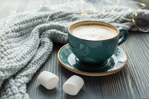 Cup of coffee, marshmallow, warm knitted sweater on wooden background. Warm lights. Cozy winter morning. Lifestyle concept. Selective focus. - Photo, image