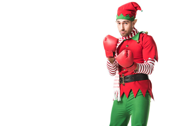 focused man in christmas elf costume wearing red boxing gloves and ready for fight isolated on white - Photo, Image