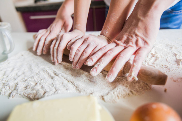Τα χέρια της μητέρας και κόρης κυλώντας πίτσα ζύμη με πλάστη μαζί στο τραπέζι της κουζίνας. - Φωτογραφία, εικόνα