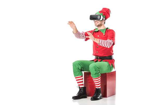 чоловік у різдвяному ельфійському костюмі сидить на коробці і носить гарнітуру віртуальної реальності ізольовано на білому
 - Фото, зображення