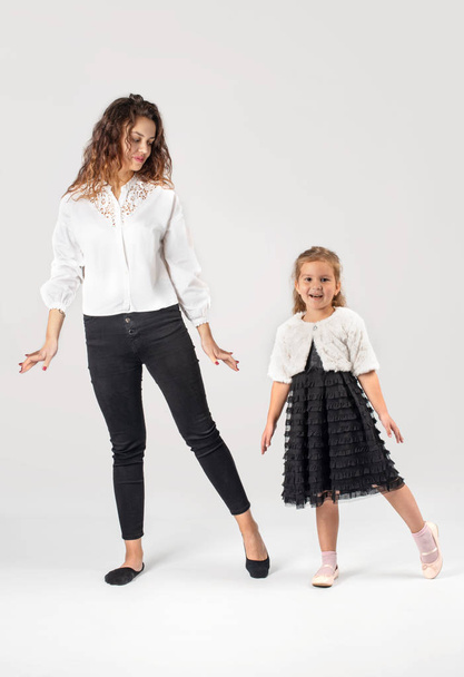 Full length portrait of a little smiling girl wearing  beautiful black  elegant dress and young woman - mother or sister.  They are dancing on a white background in the studio - Фото, изображение