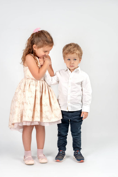 Full length portrait of a little smiling girl and boy wearing   elegant clothes.  They stand together and hold hands on a white background in the studio - Fotoğraf, Görsel