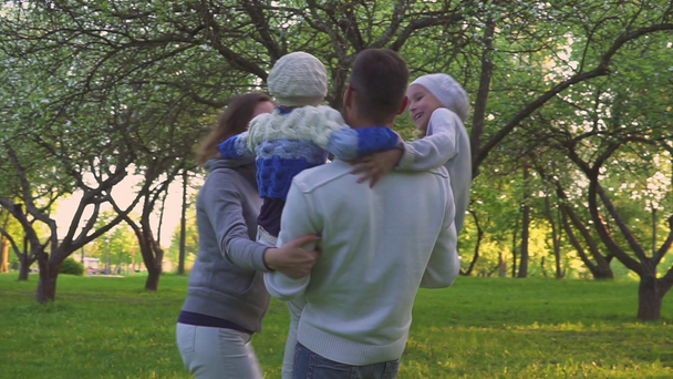 Šťastná rodina objímání na trávě. Rodiče a jejich dvě dcery jsou komplexní a na trávníku parku. Kvetoucí sad. - Záběry, video