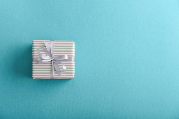 One striped  gift box with grey ribbon on blue background, top view - Zdjęcie, obraz