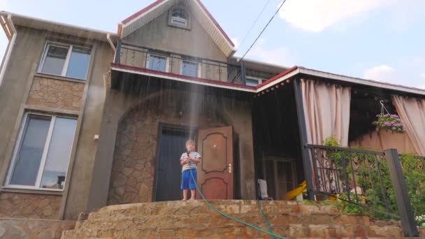 Παιδί Καθαρισμός σπιτιού με μάνικα νερού το καλοκαίρι. Χαλάρωση, παίζει με το νερό και υδροσωλήνα - Πλάνα, βίντεο