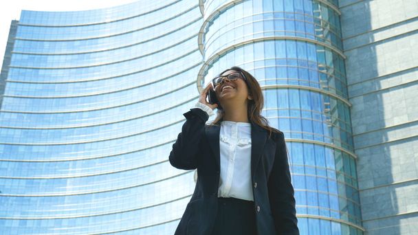 Portrait of a young beautiful business woman (female student) in a suit, glasses, smiling, successful, talking on the phone, skyscraper. Concept: new business, communication, Arab, banker, manager. - Fotografie, Obrázek
