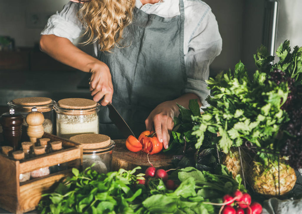 Fall seasonal vegetarian, vegan dinner cooking. Woman in linen apron cutting fresh tomatoes on concrete kitchen counter. Slow food, comfort food, healthy diet, clean eating - Fotó, kép
